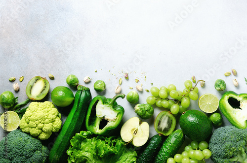 Fototapeta Naklejka Na Ścianę i Meble -  Organic green vegetables and fruits on grey background. Copy space, flat lay, top view. Green apple, lettuce, zucchini, cucumber, avocado, kale, lime, kiwi, grapes, banana, broccoli