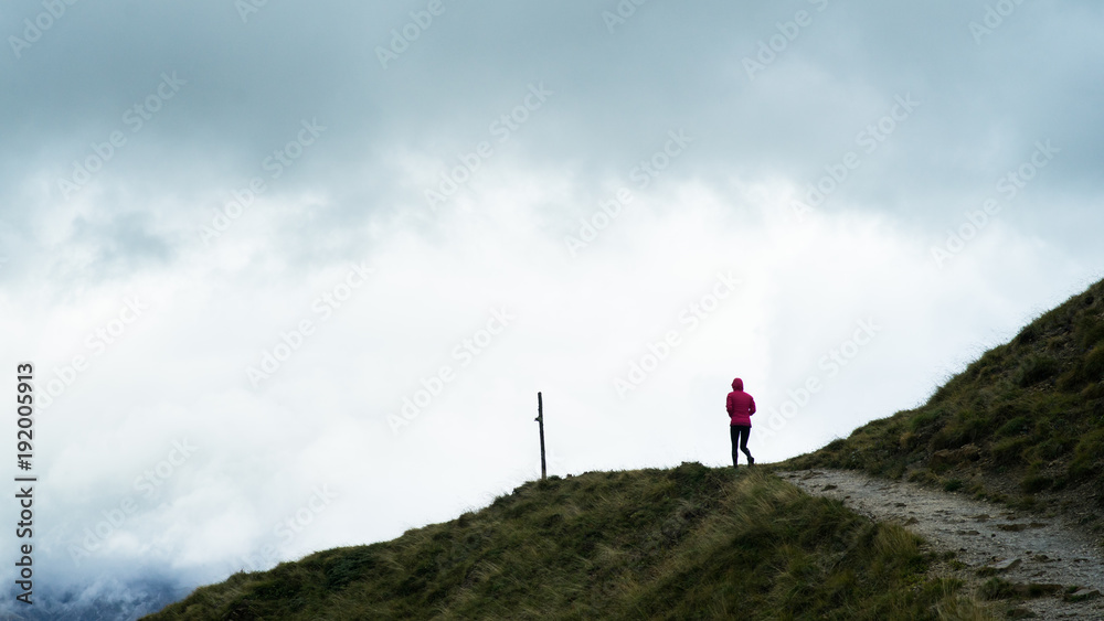 A hiker walking along a path to the top of a hill with a storm approaching in the distance