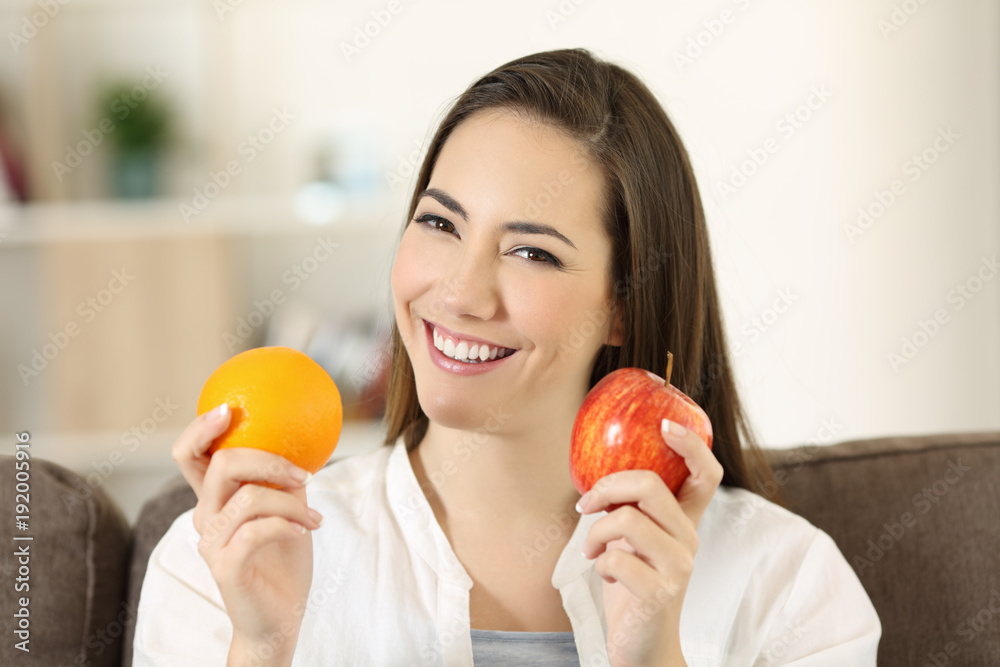 Woman holding an apple and orange looking at camera Woman holding an apple and orange looking at camera