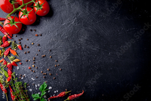 Fresh cherry tomatoes on a black background with spices with slate plate. Top view with copy space.