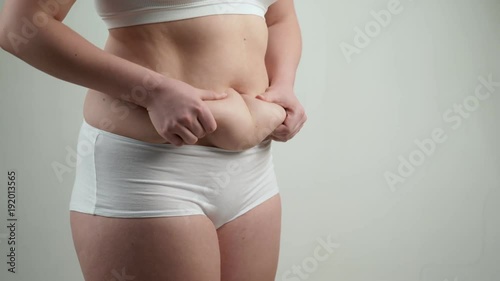 Woman in white underwear holds her belly fat.