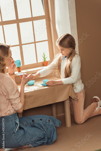 mother and adorable little daughter having tea party in cardboard house