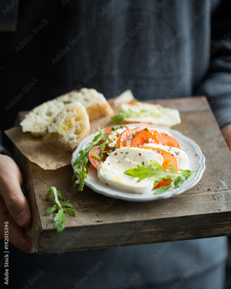 Φωτογραφία Sliced Italian cheese Mozzarella with a fresh arugula, tomatoes, olive oil, pesto sauce and bread toasts on a wooden box