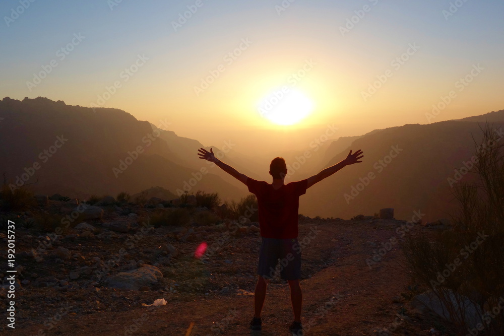 Young man standing during sunset in Canyon of Dana Biosphere Nature Reserve landscape near Dana historical village, Jordan, Middle East Young man standing during sunset in Canyon of Dana Biosphere Nature Reserve landscape near Dana historical village, Jordan, Middle East