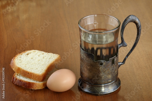 Faceted glass of hot water for tea in an ancient silver cup holder, one egg and two slices of bread