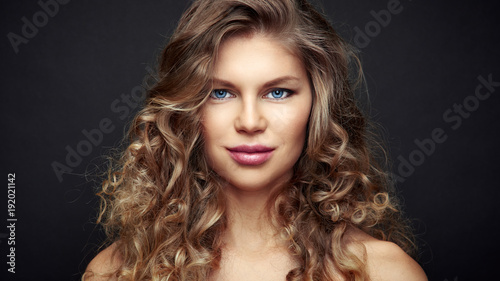 Studio portrait of young beautiful female with curly long hair over black background. 