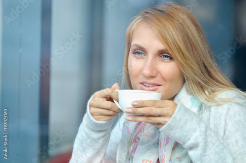 Portrait of a pensive girl drinking coffee and looking outdoors through a window
