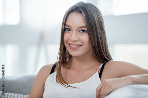 In high spirits. Good-looking exuberant long-haired young slim woman smiling and wearing a top and relaxing