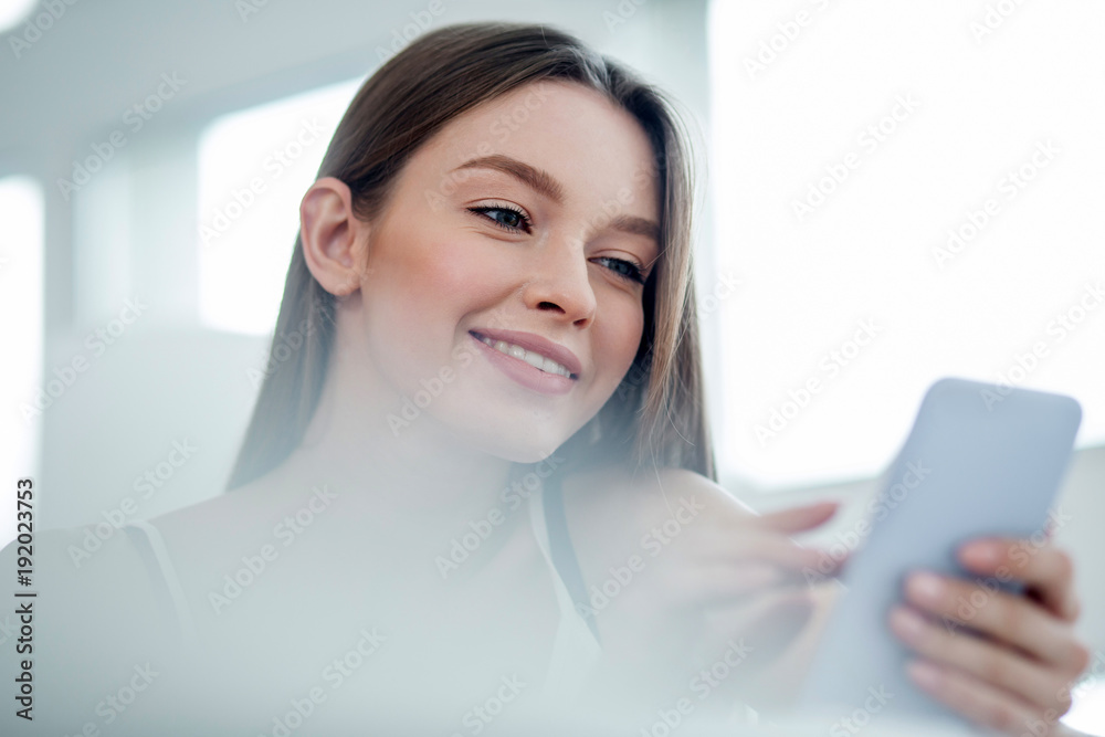Great day. Beautiful content dark-haired young woman smiling and wearing a top and typing on her phone Great day. Beautiful content dark-haired young woman smiling and wearing a top and typing on her phone