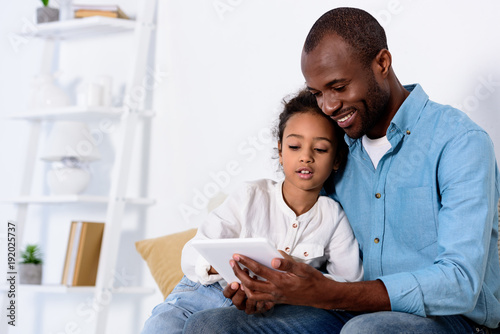 african american father and daughter watching something on tablet at home