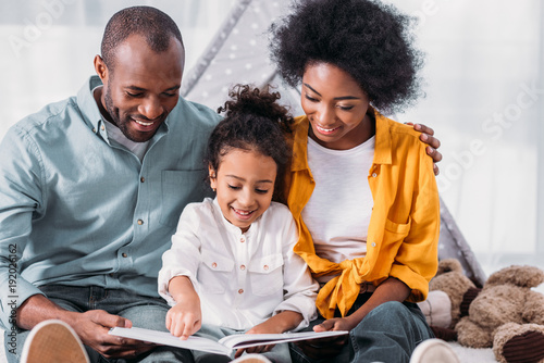 happy african american daughter reading for parents at home photo