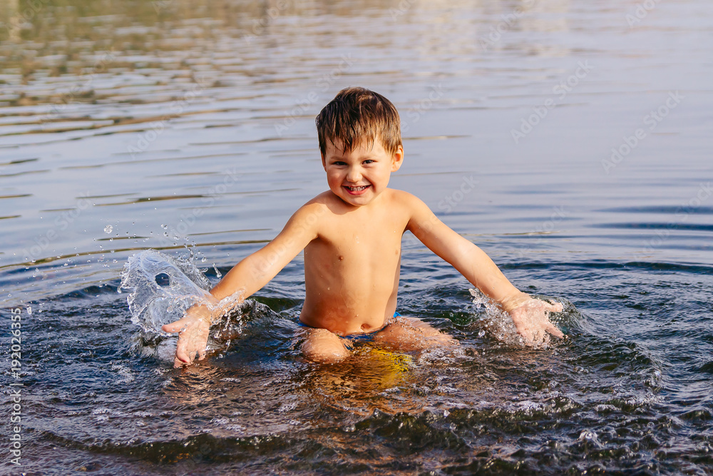 Fototapeta premium little boy splashes water . Swimming in warm lake on Sunny summer day