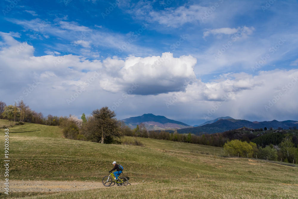 Woman cyclist in a beautiful spring landscape in the Carpathian Mountains, Transylvania, Romania with clouds and a blue sky Woman cyclist in a beautiful spring landscape in the Carpathian Mountains, Transylvania, Romania with clouds and a blue sky
