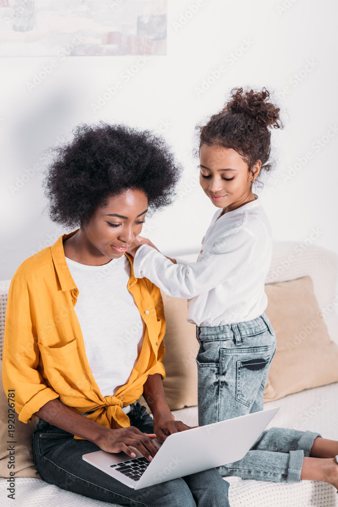 african american mother and daughter looking at laptop at home