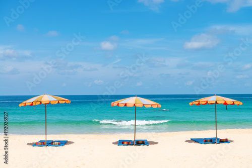 Three empty sunbeds and beach parasol sunshades on sand beach
