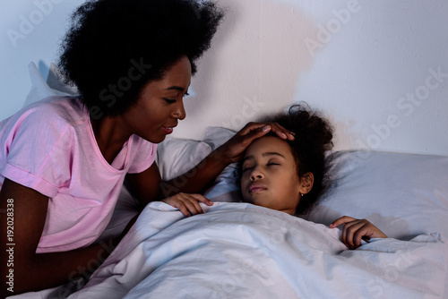 african american mother palming sleeping daughter at home