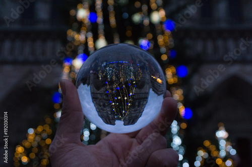 A hand holding a crystal ball for optical illusion. France landmark as the background in the night live of Paris. Known as an orbuculum, is a crystal or glass ball and common fortune telling object.