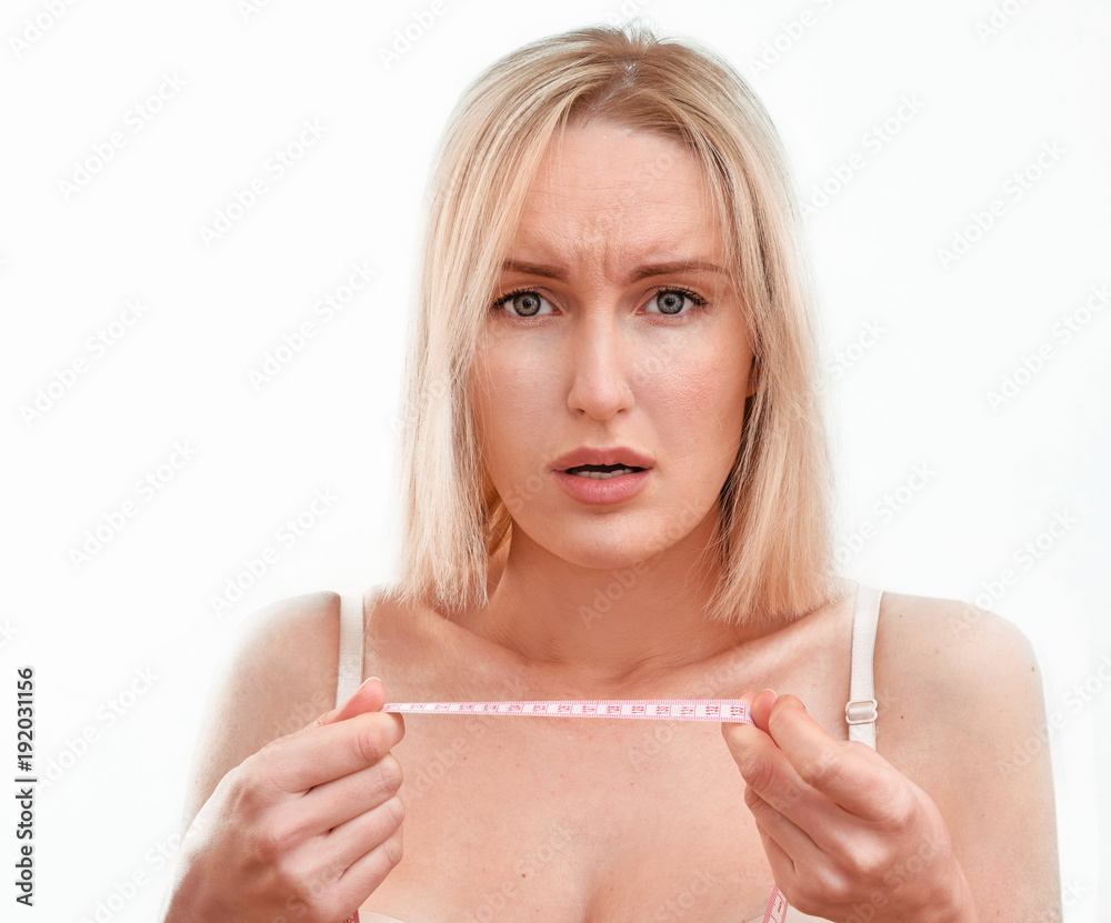 Beautiful blonde woman with clean healthy skin and big breasts is measuring  herself with a measuring