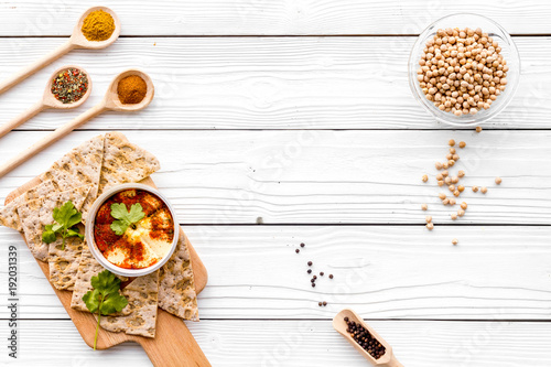 Serve hummus. Bowl with dish near pieces of crispbread on white wooden background top view copy space