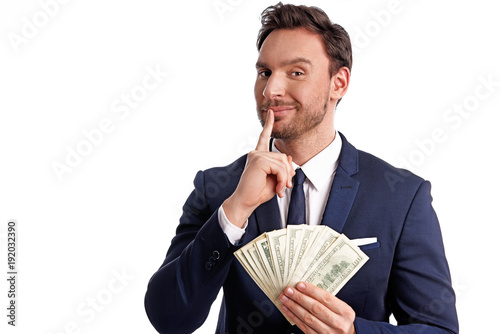 Handsome bearded young Businessman is holding a big stack of dollars and smiles isolated on a white background. Happy rich Guy in office suite with big money in his hands, he is a lucky winner