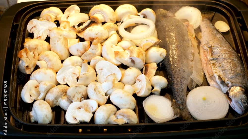 Fish, onions and mushrooms cooking on the grill and a hand is adding more onion rings Fish, onions and mushrooms cooking on the grill and a hand is adding more onion rings