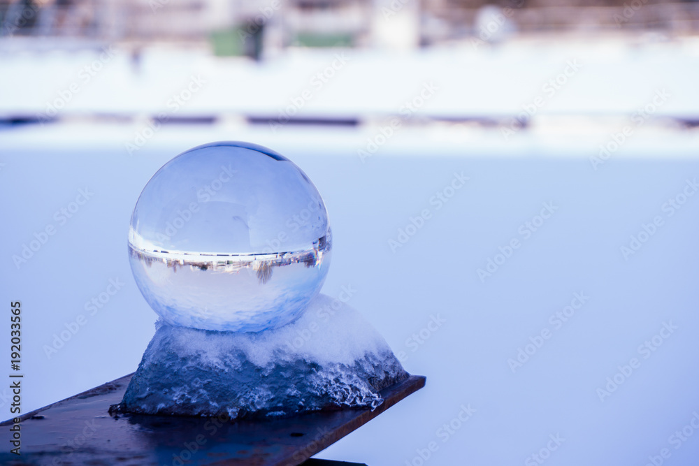 Obraz premium A crystal ball, also known as an orbuculum, is a crystal or glass ball and common fortune telling object. With a city snow background during winter in Paris, France. Used also for optical sciences. 