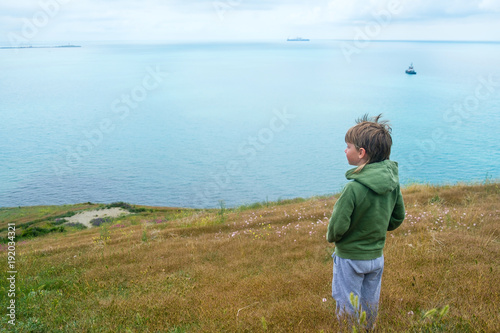 Little 6 years old boy stands on top of mountains and looking out to the sea. © familylifestyle