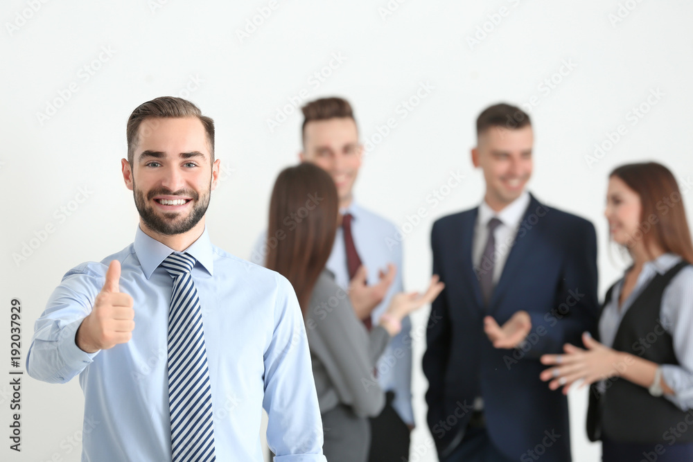 Young businessman showing thumb-up gesture and his team on background Young businessman showing thumb-up gesture and his team on background