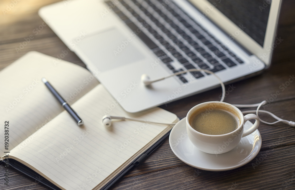 Earbuds with notebook and coffee near laptop Earbuds with notebook and coffee near laptop