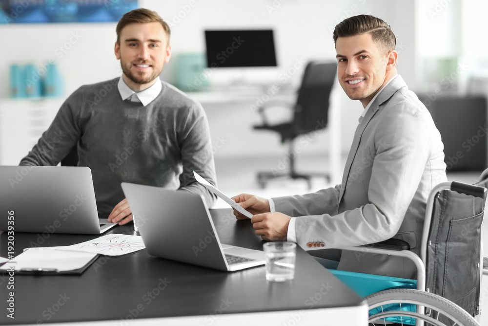 Young man in wheelchair with colleague at workplace Young man in wheelchair with colleague at workplace