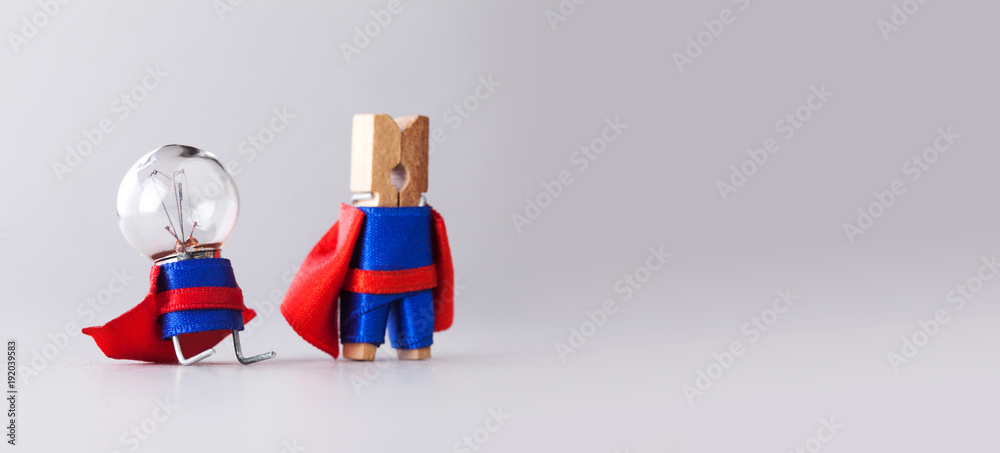 Success management creative concept. Super heroes team clothespin and light bulb, funny toy characters in blue suit and red cape. Gray background copy space. Selective focus