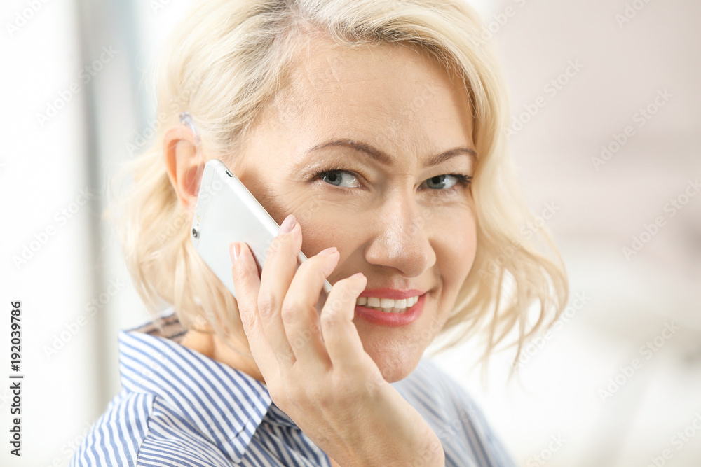 Mature woman with hearing aid talking on cell phone indoors Mature woman with hearing aid talking on cell phone indoors