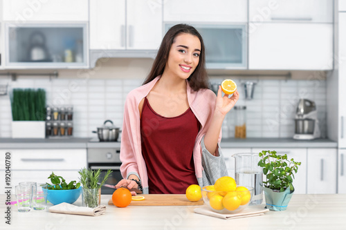 Young woman preparing tasty lemonade in kitchen