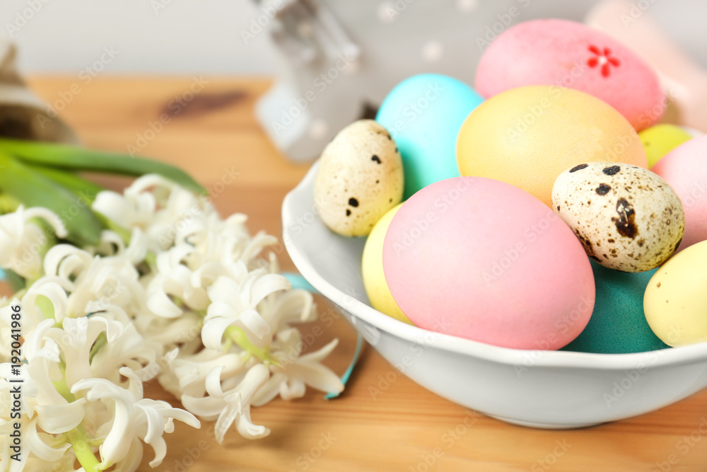 Flowers and bowl with colorful Easter eggs on table