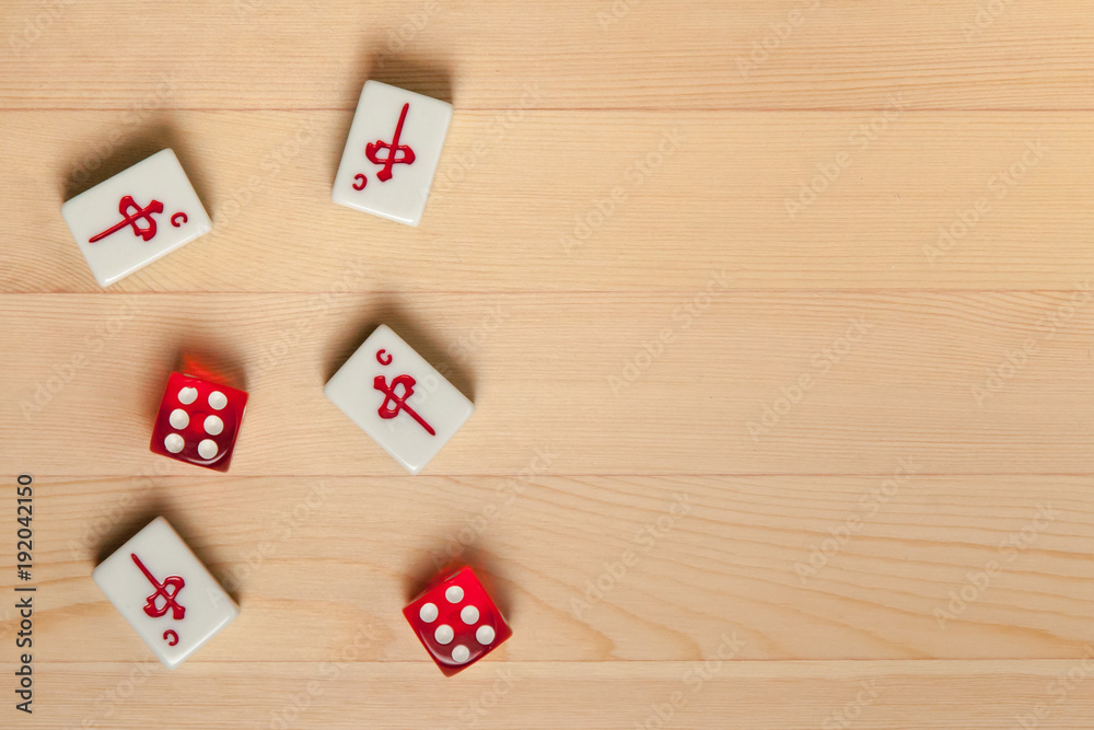 Red dice and bones (tiles) for mahjong on a light brown wooden background.