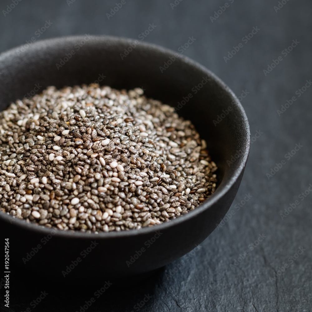 Chia seeds in a black metal bowl on a black textured board. Macro photography. Chia seeds in a black metal bowl on a black textured board. Macro photography.