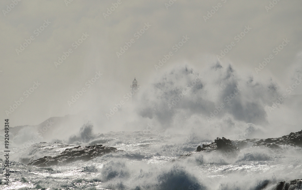 Rough sea, big wave when breaking on the coast and silhouette of lighthouse in background, Telde, Canary islands