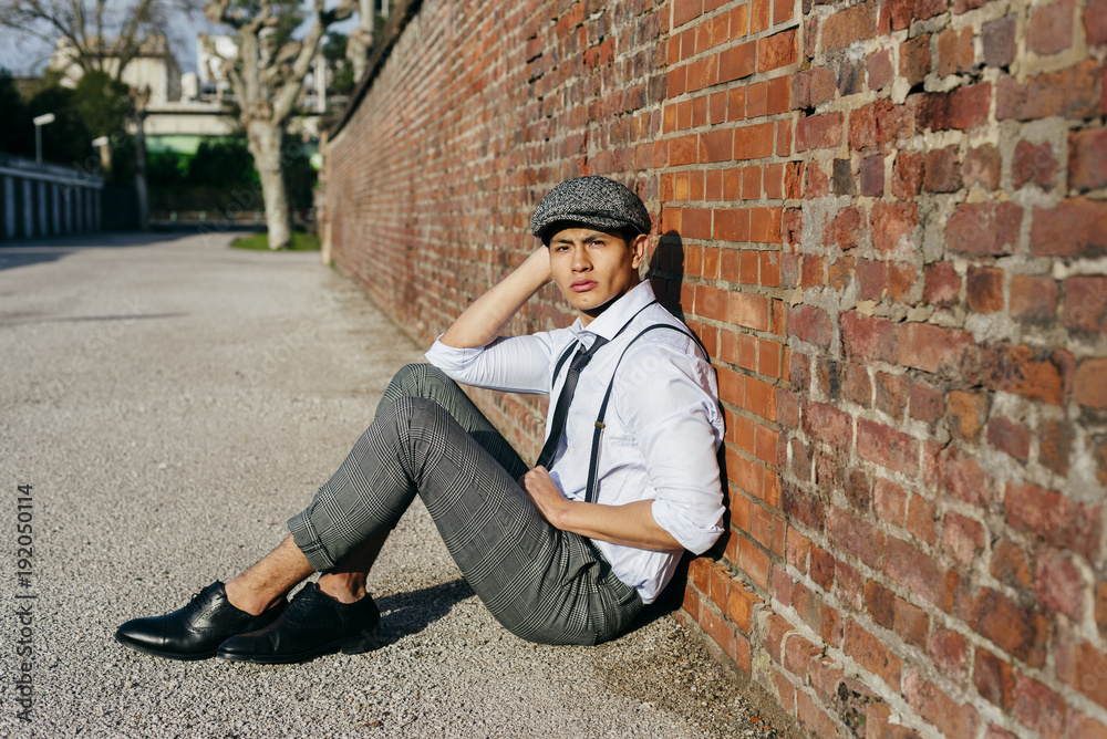 Fashionable man in cap sitting at brick wall