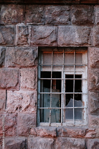 Abandoned window with bars in pink tuf wall