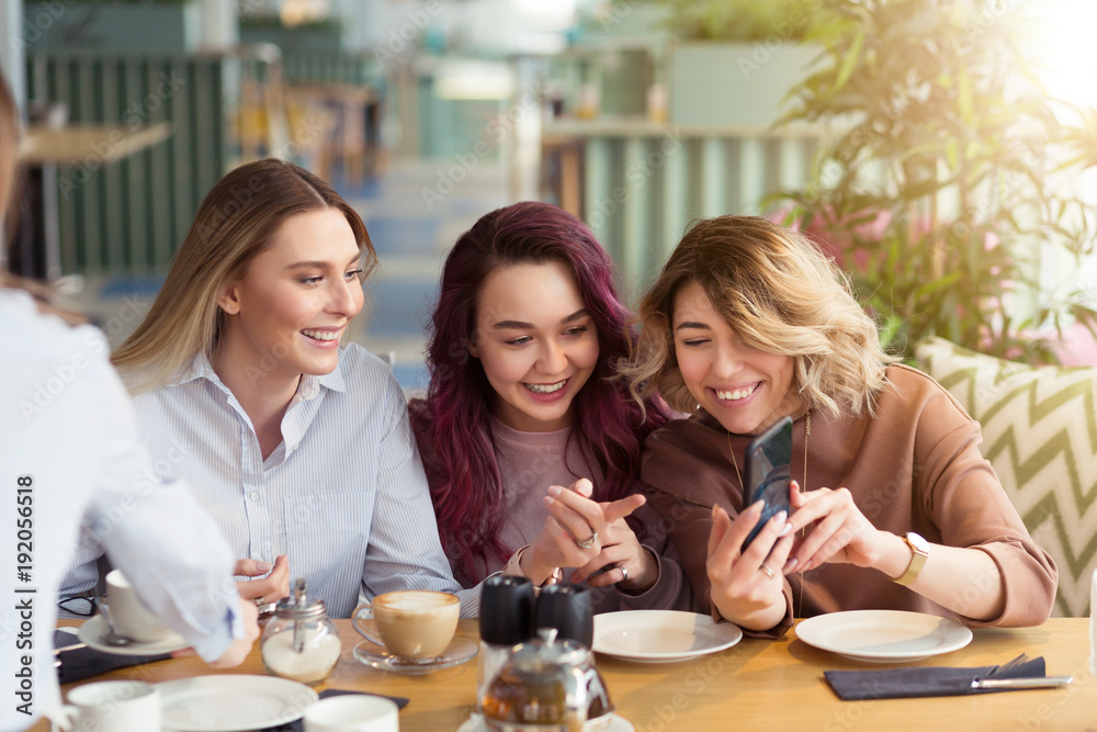 Young beautiful girls taking selfie photo at cafe or coffee shop. Happy women friends having fun, talking together and looking photos at mobile phone. Female friendship, communication concept