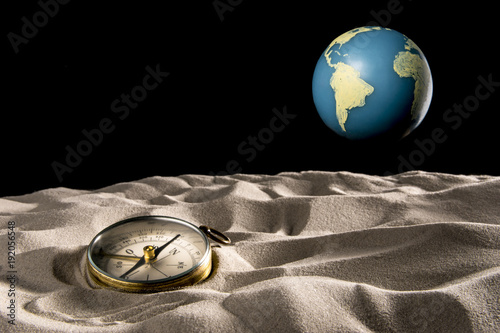 Compass on the desert sand and Earth in the black sky. With copy space text. Studio Shot.