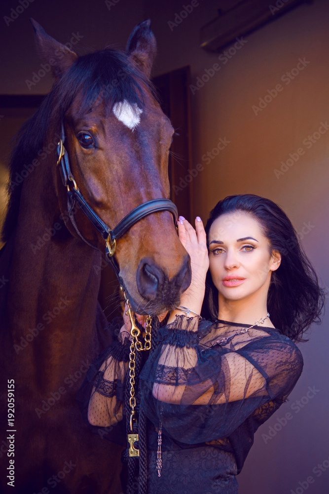Gorgeous stylishly dressed woman in dark lace boho style dress and gold jewelry with a thoroughbred horse. The concept of love human and animals, horses and rider lifestyle 