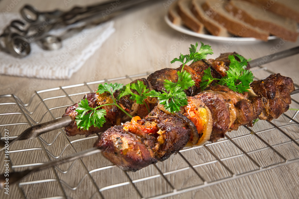Kebabs on skewers. Roasted meat, tomatoes, pepper, parsley and onion on the white dish with vegetables on the wooden table.