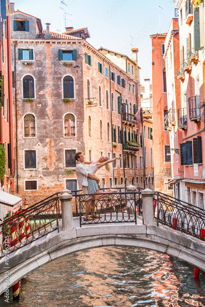 Fototapeta premium Romantyczna para na podróż poślubną w Wenecji spaceru na moście. Kochankowie romans skaczący w miłości mężczyzna i kobieta obejmując się nawzajem. Ulice letnie wakacje w Europie, Włochy.
