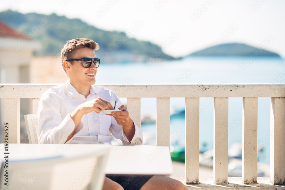 Young successful business man enjoying espresso coffee beverage in sunny marine panoramic cafe.Handsome entrepreneur drinking coffee on a luxury exotic seaside vacation.Leisure and accomplishment. Young successful business man enjoying espresso coffee beverage in sunny marine panoramic cafe.Handsome entrepreneur drinking coffee on a luxury exotic seaside vacation.Leisure and accomplishment.