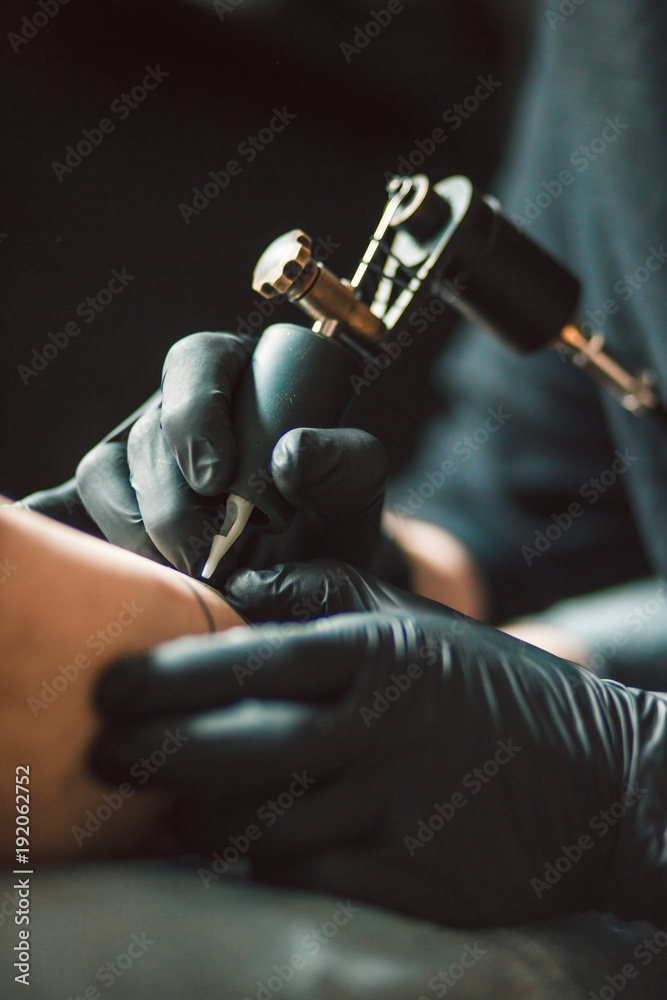 Naklejka premium Close up tattoo artist demonstrates the process of getting black tattoo with paint. Master works in black sterile gloves.