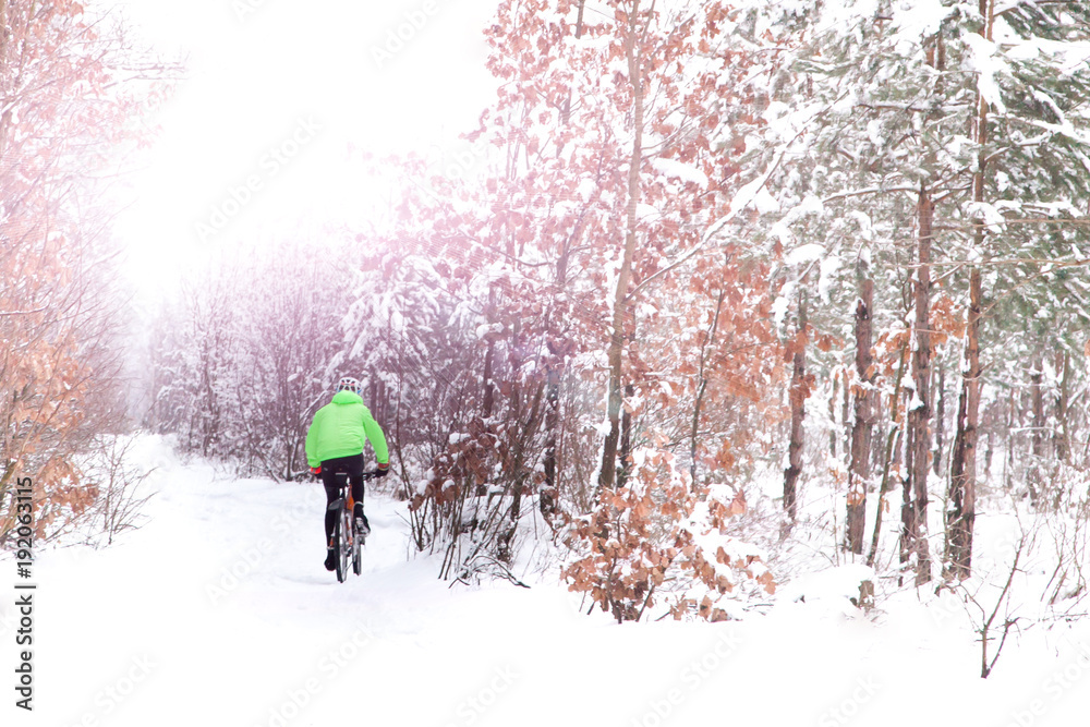 Snow biker cyclist in green rides snow mountain cross country bike in beatiful winter snowy frosty forest. Winter snow bike concept background.