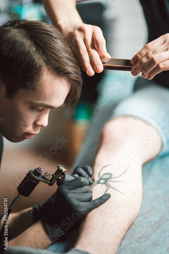 Close up image of the tattoo male artist makes a tattoo on a female leg.
