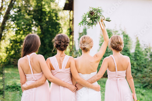 bride standing with her back  and raised hand with a bouquet  in the embraces of three bridesmaids in pink dresses transformer  photo