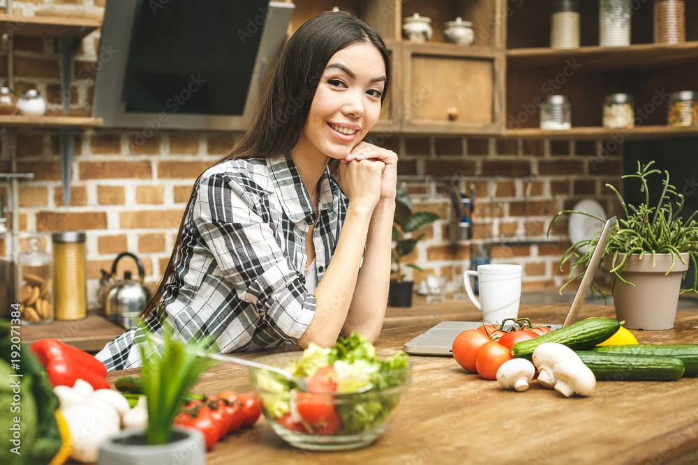 Young beautiful woman with laptop on kitchen finding recipes and smiling. Food blogger concept. Close-up.